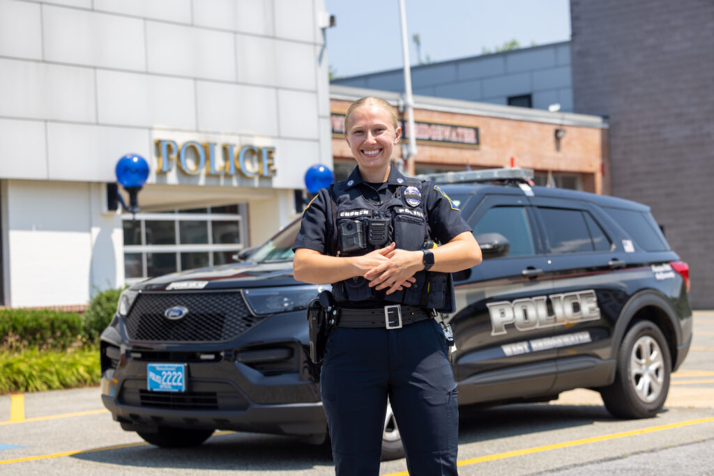 A female officer stands in front of a cruiser.